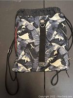 Full view of the backpack showing the tropical leaf print, drawstring cords, and black strap.