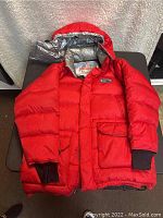 Front view of red First Down mountain jacket showing hood, pockets, and ribbed cuffs.