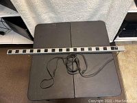 Long metal multiple outlet power strip with 15 outlets and attached power cord, placed horizontally on black surface.