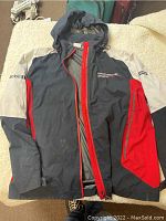 Front view of Porsche jacket showing black main body with red and white sleeves, Porsche Motorsport logo on chest, and detailed zipper.
