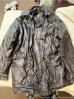 Full view of the dark brown genuine leather jacket laid flat showing front zipper, snap buttons, and drawstring waist.