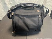 Front view of the SwissGear black laptop bag with shoulder strap and front zippered pocket, on a black surface with a soft light background.