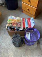 Box full of books including cookbooks and non-fiction seen with two metal display stands on the floor