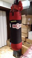 Front and side view of red and black Ring Side boxing bag in basement room with cardboard boxes in background.