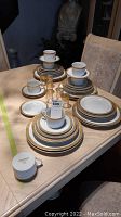 Full display of china set including stacked dinner plates, side plates, cups, and glasses arranged on a table.