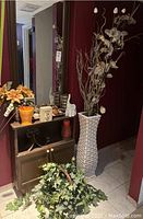 Overview of decor items including orange basket with faux flowers, elephant sculpture, candles on tray, and tall white vase with faux flowers and branches against burgundy wall