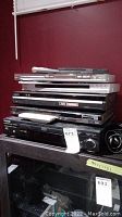 Stack of five player devices with some remotes placed on top showing multiple brand labels