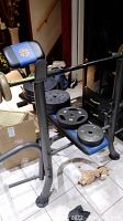 Marcy weight bench with black and blue padding and metal frame, showing barbell rack and weight plates stored on the bench and floor nearby.