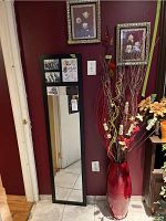 Photo showing black framed mirror, floral prints on wall above, and red vase with floral arrangement on floor