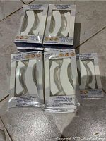 Five packs of Satin Smooth EZ Grip non-woven cloth contour strips laid out on a tiled floor, showing the packaging and curved shape of strips inside.