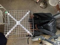 Metal stool with square grid seat showing remnants of orange paint on metal, photographed with black backpack beside it