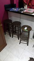 Three dark brown wooden stools seen from a slight angle, showing minor surface scratches and the stool design with round seats and four legs.