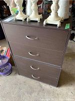 Front view of brown four drawer storage cabinet with silver metal handles. Top surface holds decorative white lamp bases.