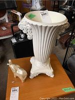 Full view of large white decorative vase with small elephant figure beside it on a wooden table