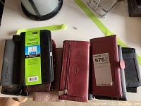 Photo showing multiple wallets, card cases, a daytimer and glasses case placed side by side in various colors including black, brown and red shades.