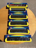 Photo showing 7 Athearn model train miniatures in original boxes laid out on a wooden surface outdoors.