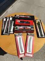 Overview of all items on a round wooden table, showing boxed locomotives, tanker car set, and boxed track accessories arranged together.