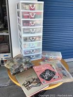 Photo of a plastic storage unit with eight translucent drawers containing sewing supplies on a table along with two clear button organizers and three sewing/crafting books.