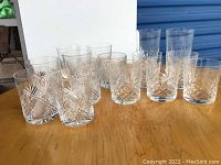 Full view of 12 crystal tumblers on a wooden surface showing variation in cut patterns and sizes.