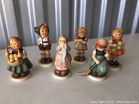 Six hand-painted Hummel figurines of children on round white bases showing slight wear and age-related imperfections.