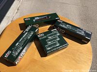 Four original Kato model train boxes with green design displayed on table.