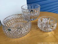 Set of three clear lead crystal bowls on wooden surface, showing their size difference and design.
