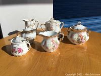 Set of five porcelain china items displayed on wooden surface under natural light showing floral patterns and gold accents.
