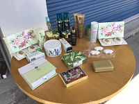 Overview photo showing assorted soaps, skincare jars, tubes, perfume, and decorative soap bars arranged on a wooden round table outdoors.