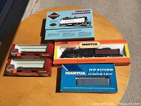 Photo showing all included Mantua model train kits arranged on a round table, featuring the locomotive, a double-pack of rolling stock kits, and the blue refrigerator car kit.