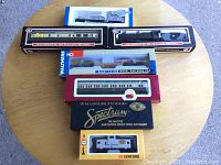 Top-down view of six boxed model railroad cars including Walthers, Bachman Spectrum, and others on round table showcasing the lot contents.