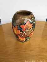 Moorcroft vase with vibrant orange flower and leaf pattern shown from one angle