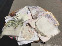 Overview of assorted embroidered and needlepoint linens spread out on a surface, showing various sizes and designs.