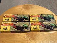 Four boxed Roundhouse model train kits stacked on a wooden round table including colorful vintage steam locomotive graphics on packaging.