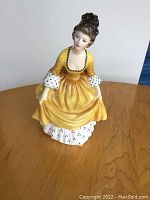 Front view of Royal Doulton figurine showing detailed face, hair and yellow dress with white polka dot accents.