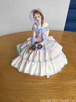 Front view of Royal Doulton 'Daydreams' young woman figurine seated wearing pastel pink and blue dress and bonnet with flowers.