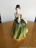Front angled view of Royal Doulton Figurine HN 2368 in green dress holding a yellow flower.
