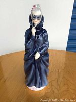 Front view of Royal Doulton Maxine figurine in glossy dark blue cloak holding a mask to face.