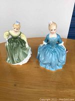 Two Royal Doulton porcelain figurines from front view, showing detailed dresses and hair ribbons.