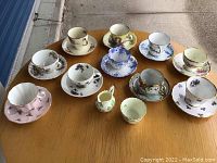 Wide angle photo of all ten teacups and saucers on a table showing assorted floral patterns and shapes