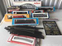 Overview of the lot showing multiple model train cars in boxes, curved track sections, and the Atlas curved chord truss bridge box in the back.