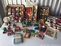 Overview of lot showing multiple boxes of glass ornaments, village houses, tinsel, snow globe and ephemera.