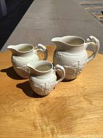 Full view of the three Wedgwood creamers on a wooden surface outside, showing size differences and relief detail.