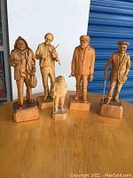 Front view of all five wooden carved figures arranged side by side on a wooden surface against a white and blue background.