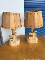 Pair of wooden table lamps on wooden surface, each with a squirrel carved base and wooden slat shade with black stitched accents.