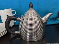 Ribbed silver plated vintage tea pot with black handle and finial shown on blue background.