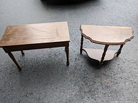 Photo showing both wooden furniture accent pieces on outdoor pavement, highlighting the rectangular piano bench and demi lune side table with scalloped edges and lower shelf.