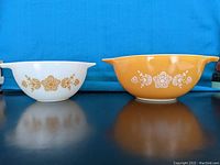 Photo showing both Pyrex mixing bowls side by side, one white and one golden yellow, with floral patterns.
