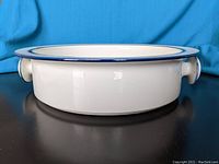 Side view of round white ceramic vegetable bowl with visible blue rim and handle on the right side.