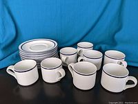 Set of 8 white cups with blue rims paired with 8 matching saucers arranged together showing quantity and condition.
