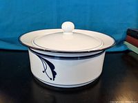 Side view showing the blue floral pattern and lid with knob handle, on a dark surface with a blue backdrop.